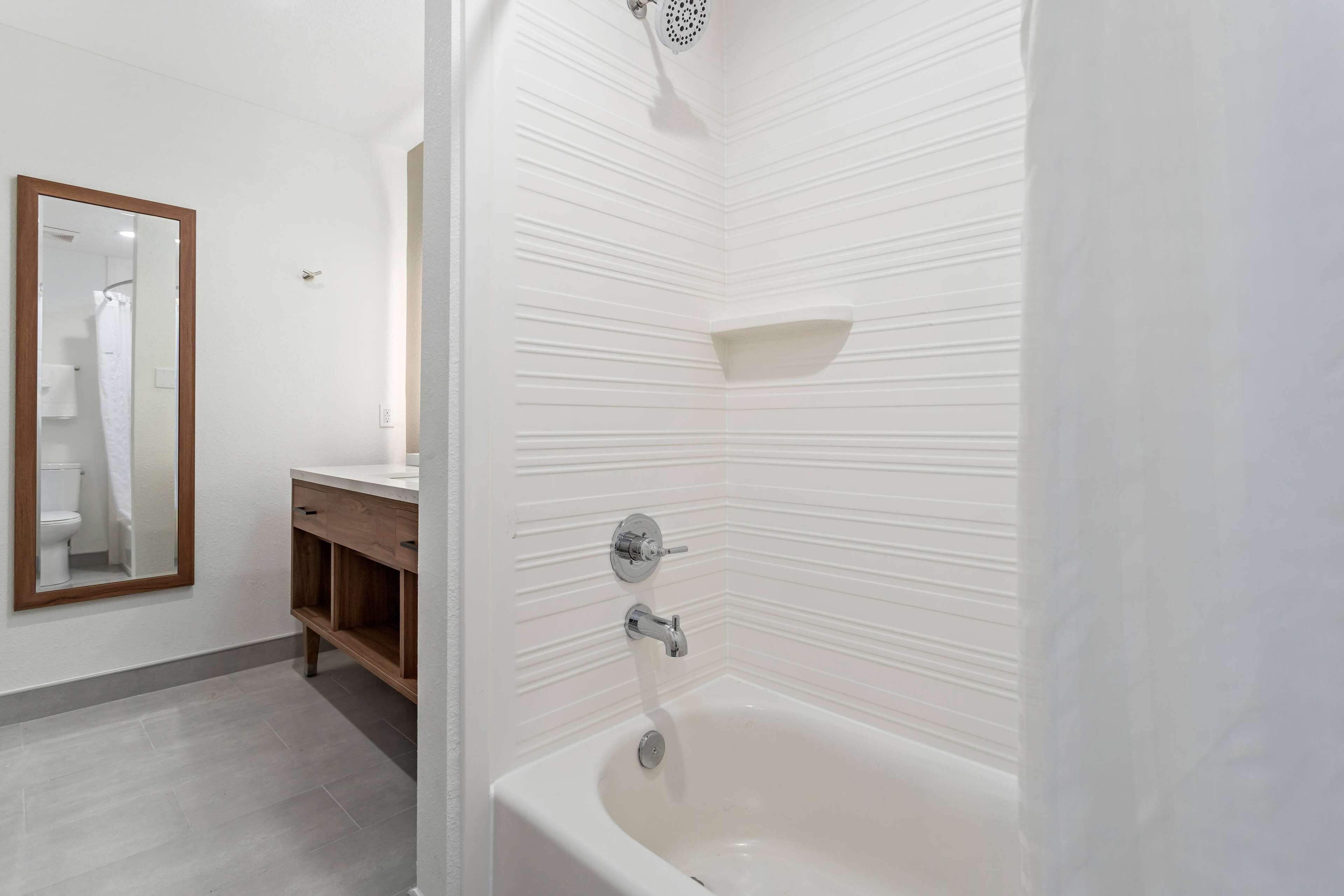 A modern bathroom with a white bathtub, a wooden vanity, and a large mirror.