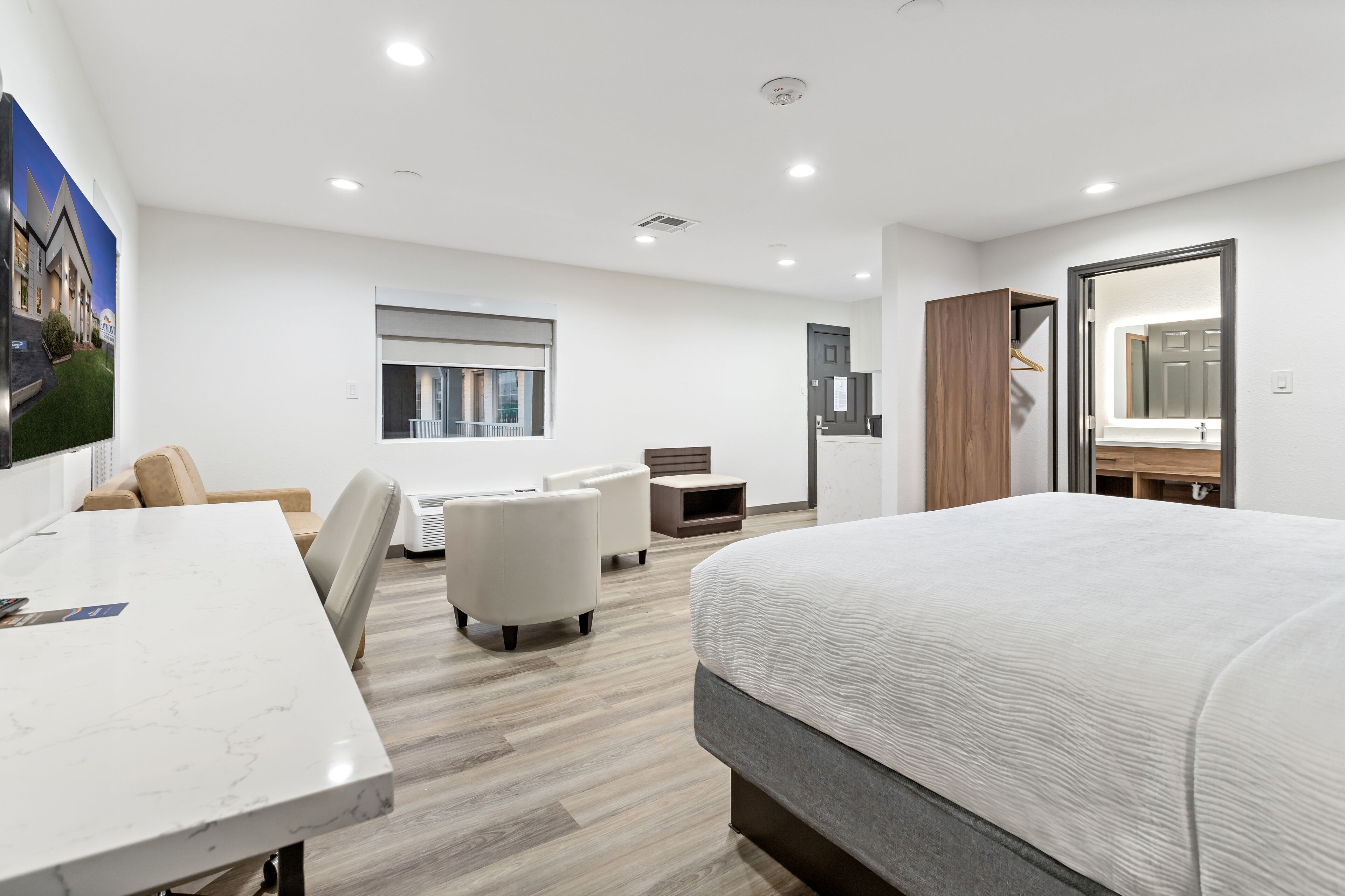 A modern hotel room with a large bed, a desk, a chair, a sofa, and a small table.
