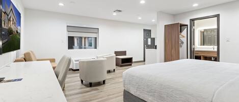 A modern hotel room with a large bed, a desk, a chair, a sofa, and a small table.