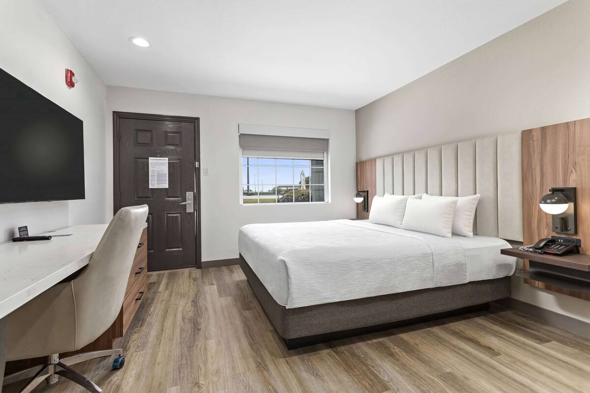 A hotel room with a bed, desk, chair, and a television.