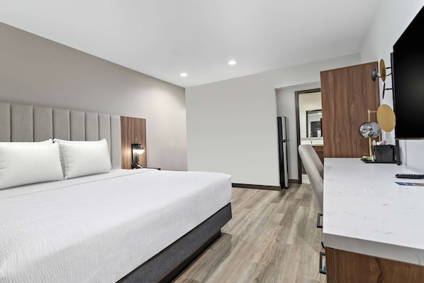 A modern hotel room with a large bed, a desk, and a mirror.
