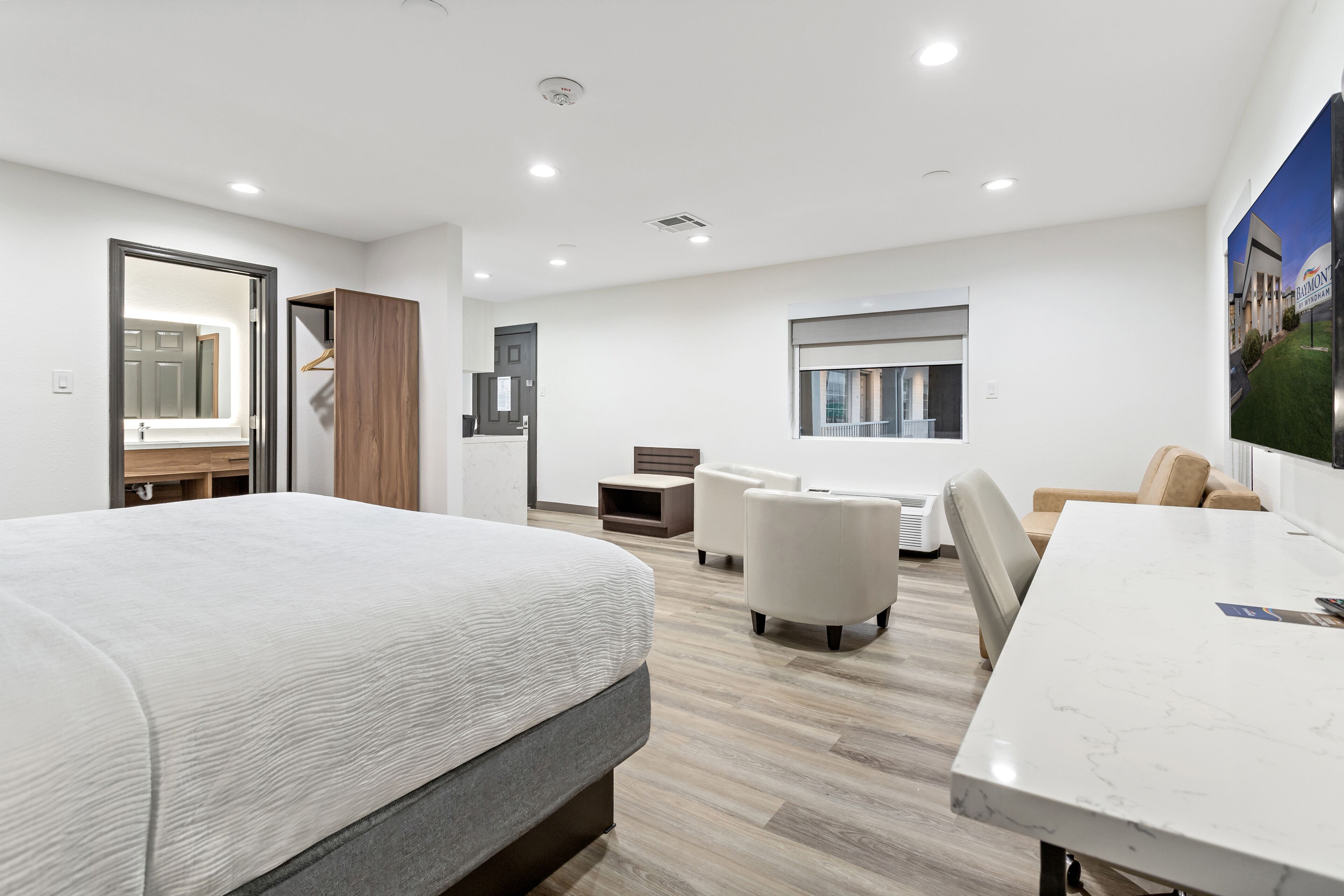 Un hotel moderno con una cama, una mesa de comedor, dos sillones, un sofá, una mesita y un espejo grande.