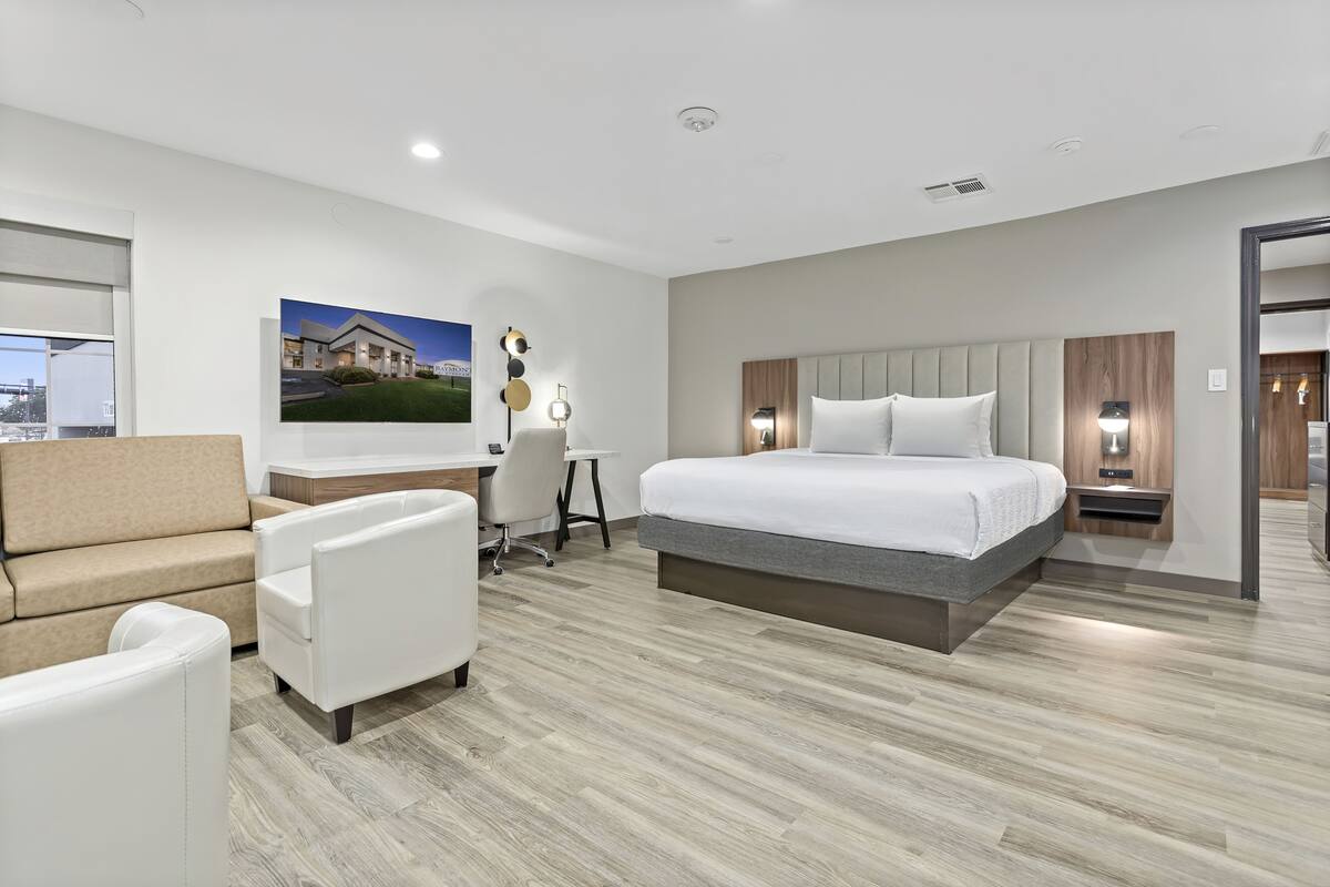 A modern hotel room with a large bed, a desk, a sofa, and a chair.