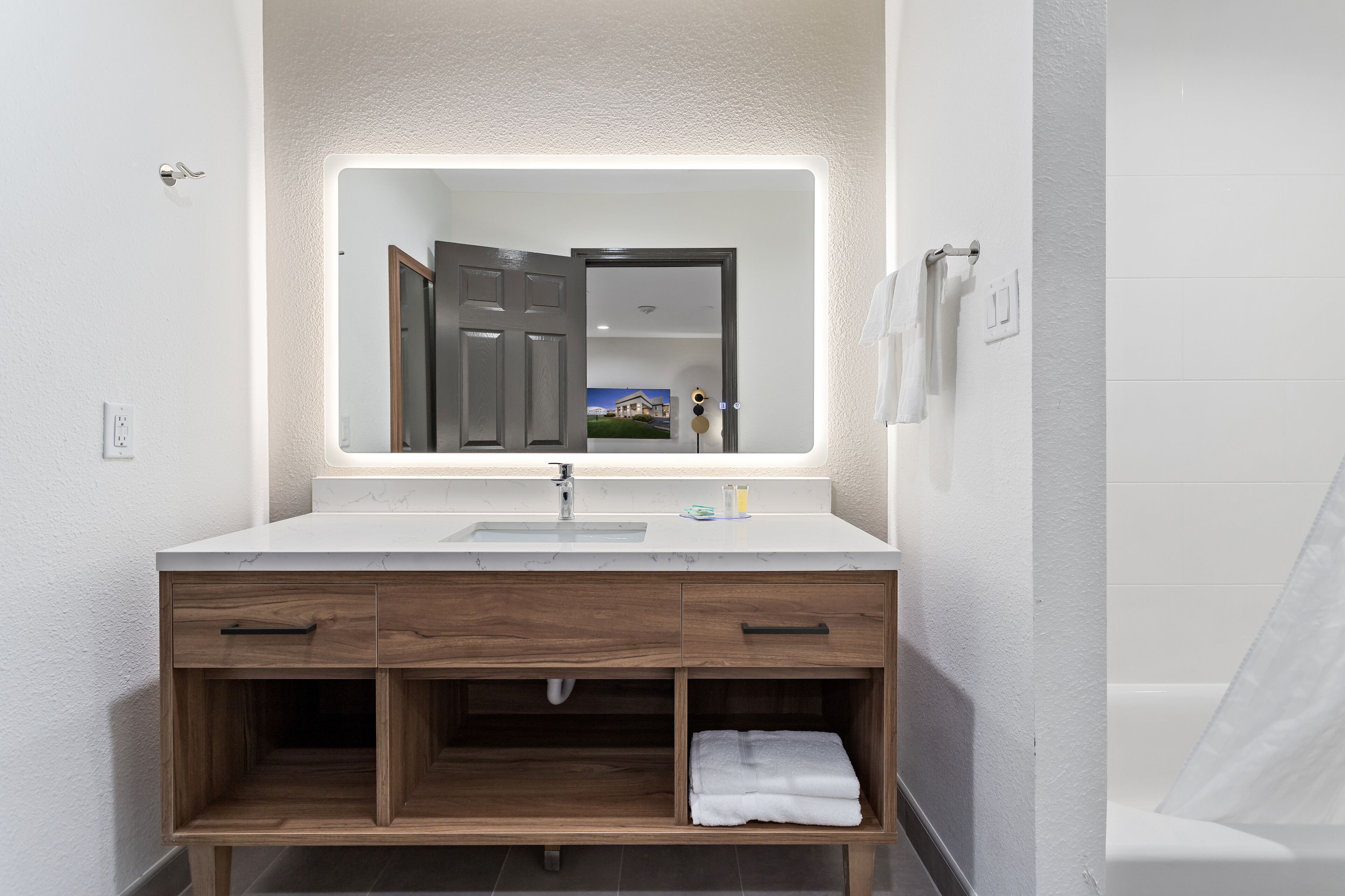 A modern bathroom with a white vanity, a large mirror, and a visible door leading to another room.