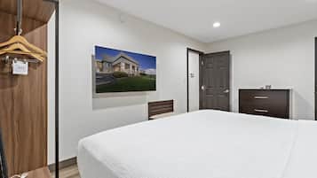 Habitación de hotel con una cama grande, un armario de madera, un escritorio con cajones, una silla y un cuadro en la pared.
