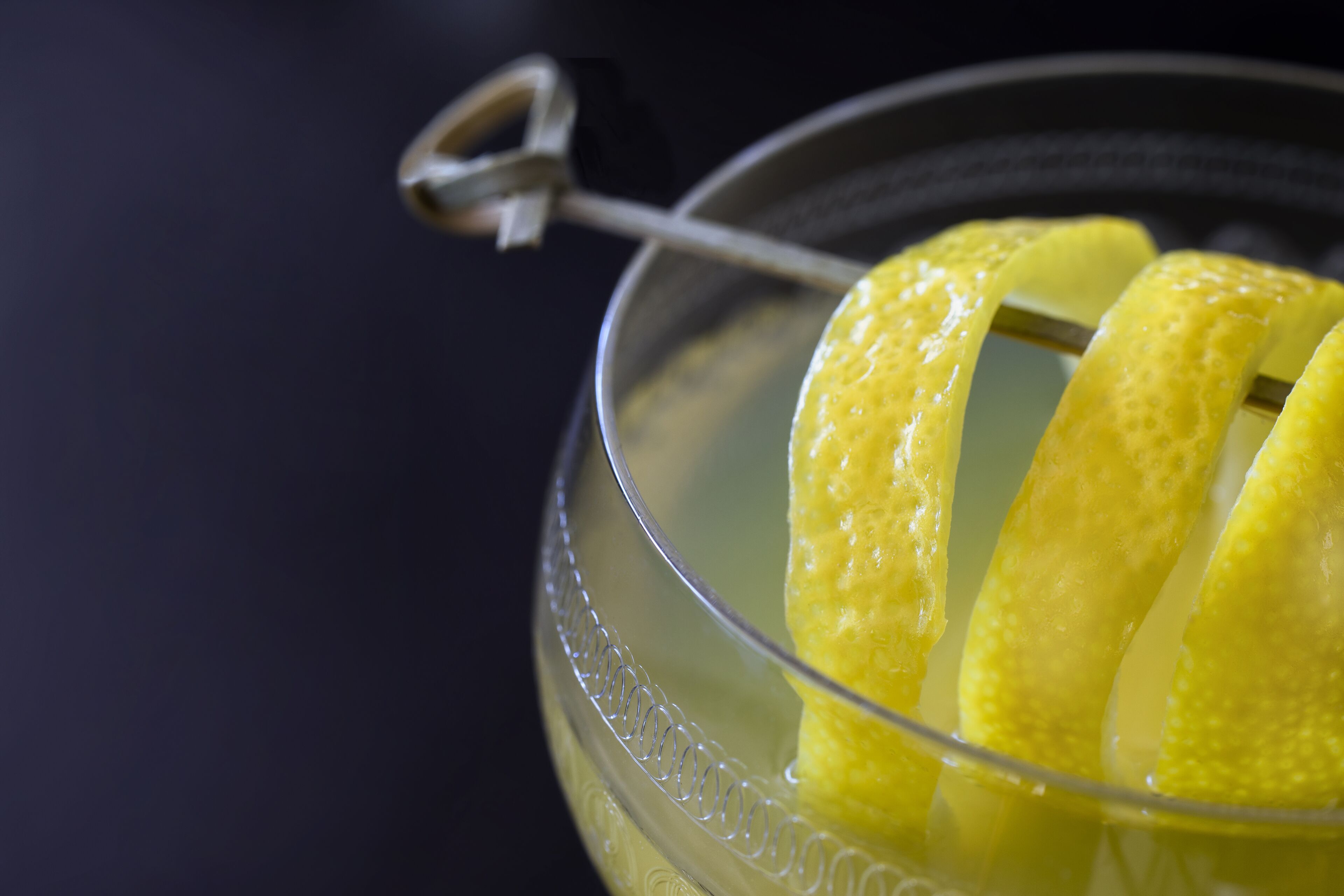 A clear glass bowl with a metal spoon, containing a yellow substance, possibly a lemon, with a dark background.