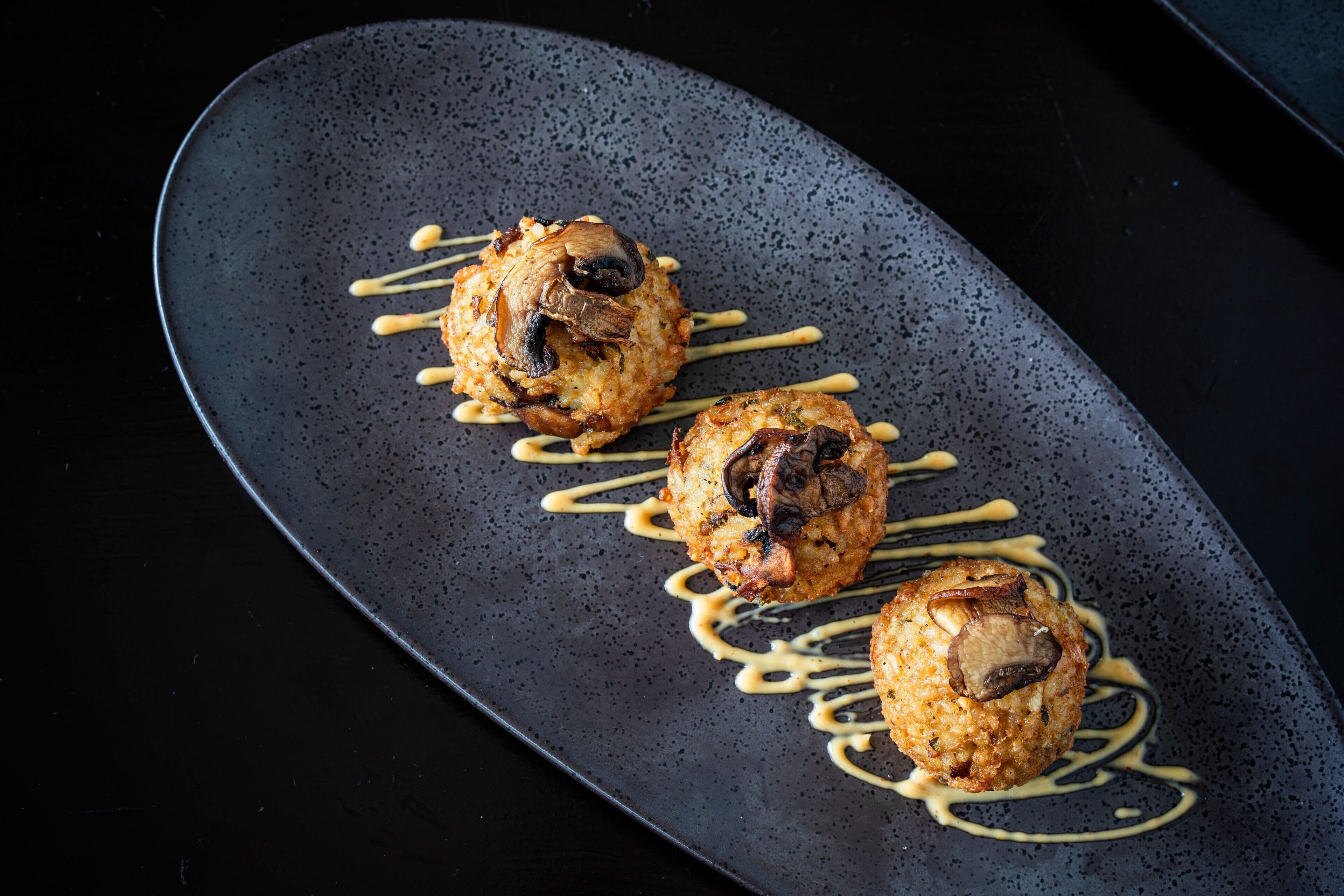 Un plato oscuro y moteado con tres piezas redondas de color marrón dorado y salsas rociadas.