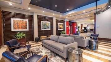 A modern lobby with a grey sofa, leather chairs, a patterned rug, and framed artwork on the walls.