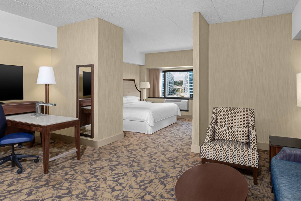 A hotel room with a bed, a desk with a lamp, a chair, and a television.