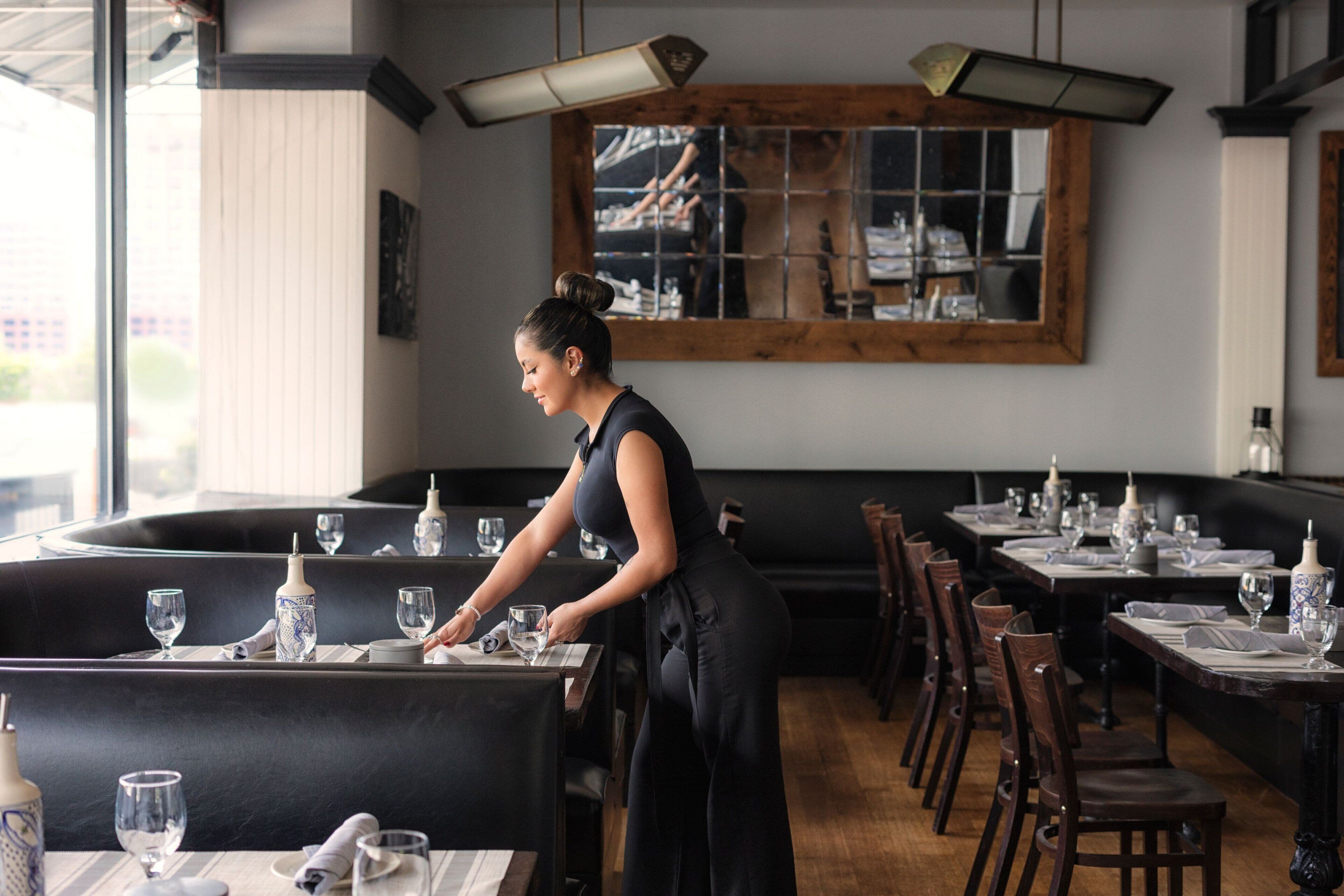 Um restaurante com decoração moderna, apresentando um balcão comprido e cabines. Mesas montadas com copos de vinho e pratos.
