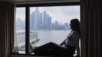 A person sitting by a window overlooking a cityscape with a river and buildings.