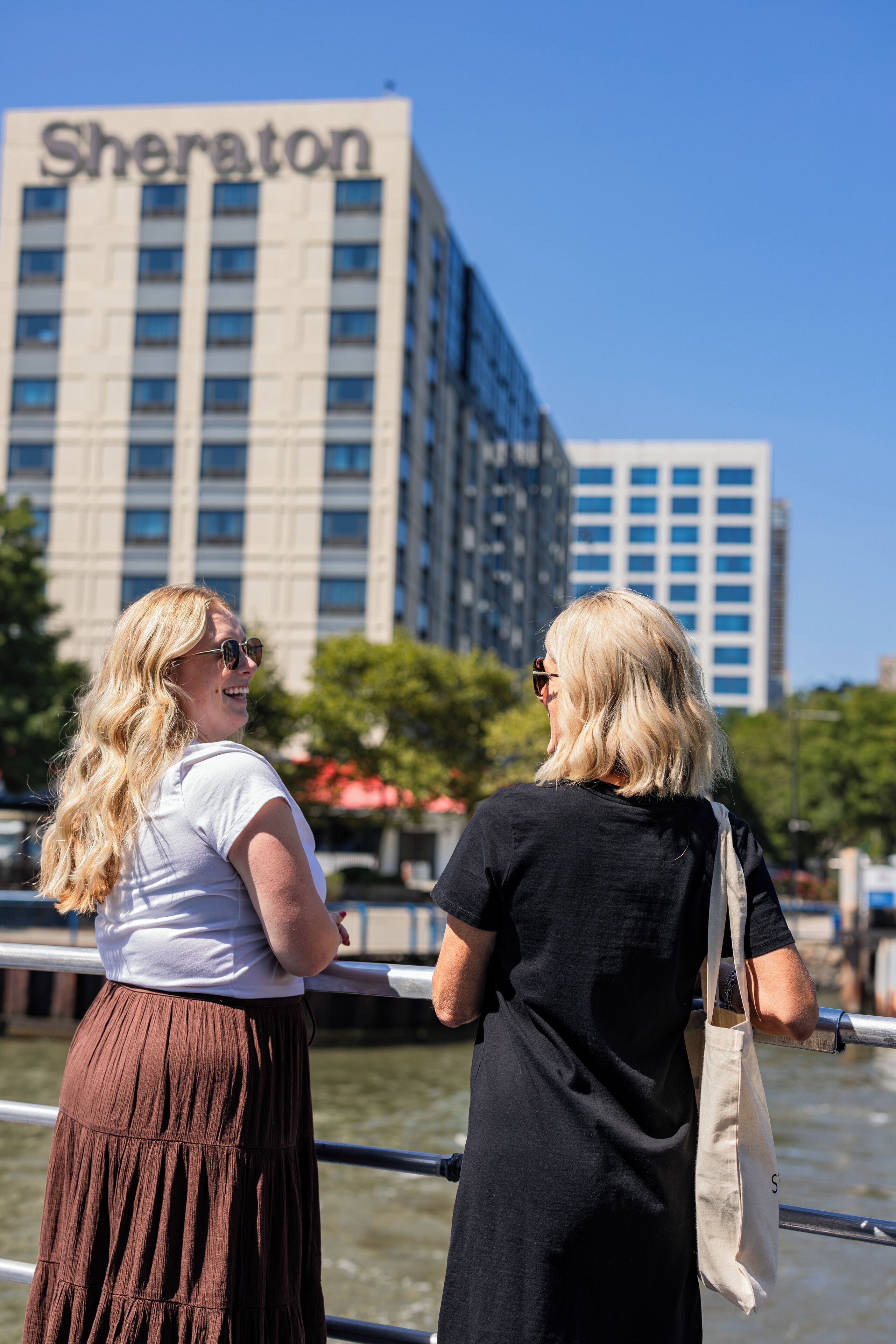Deux personnes se tiennent près d’une rambarde, avec un hôtel Sheraton en arrière-plan.