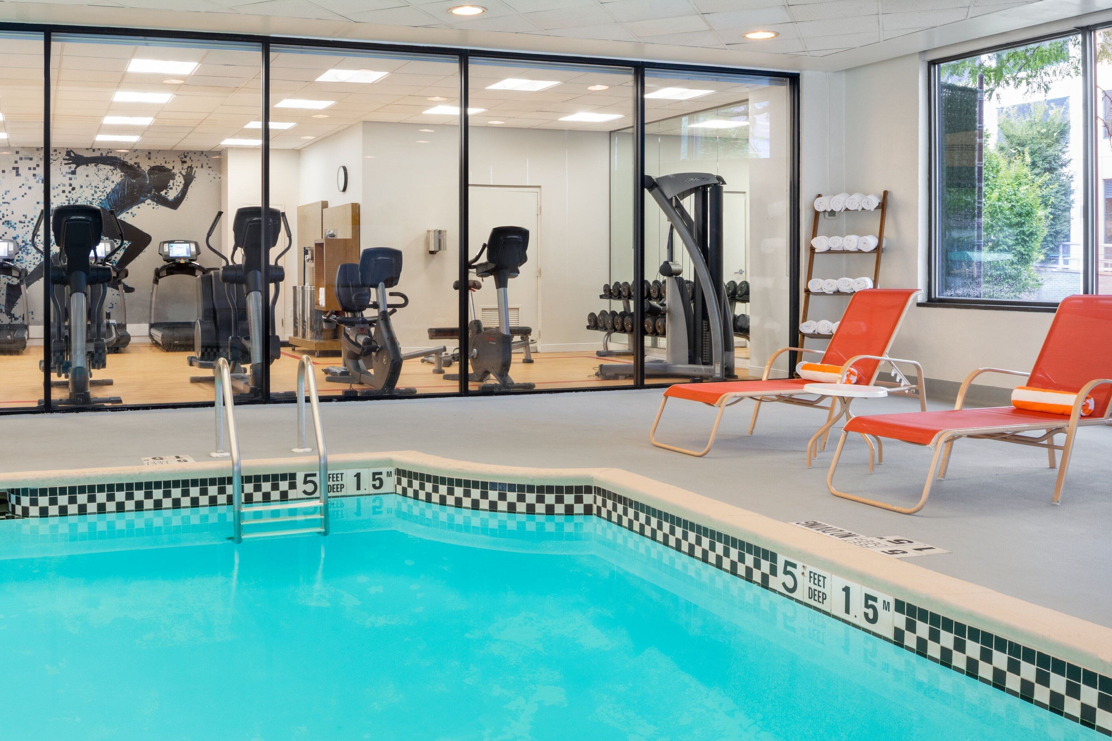 An indoor swimming pool with exercise equipment, lounge chairs, and a view of the outdoors.