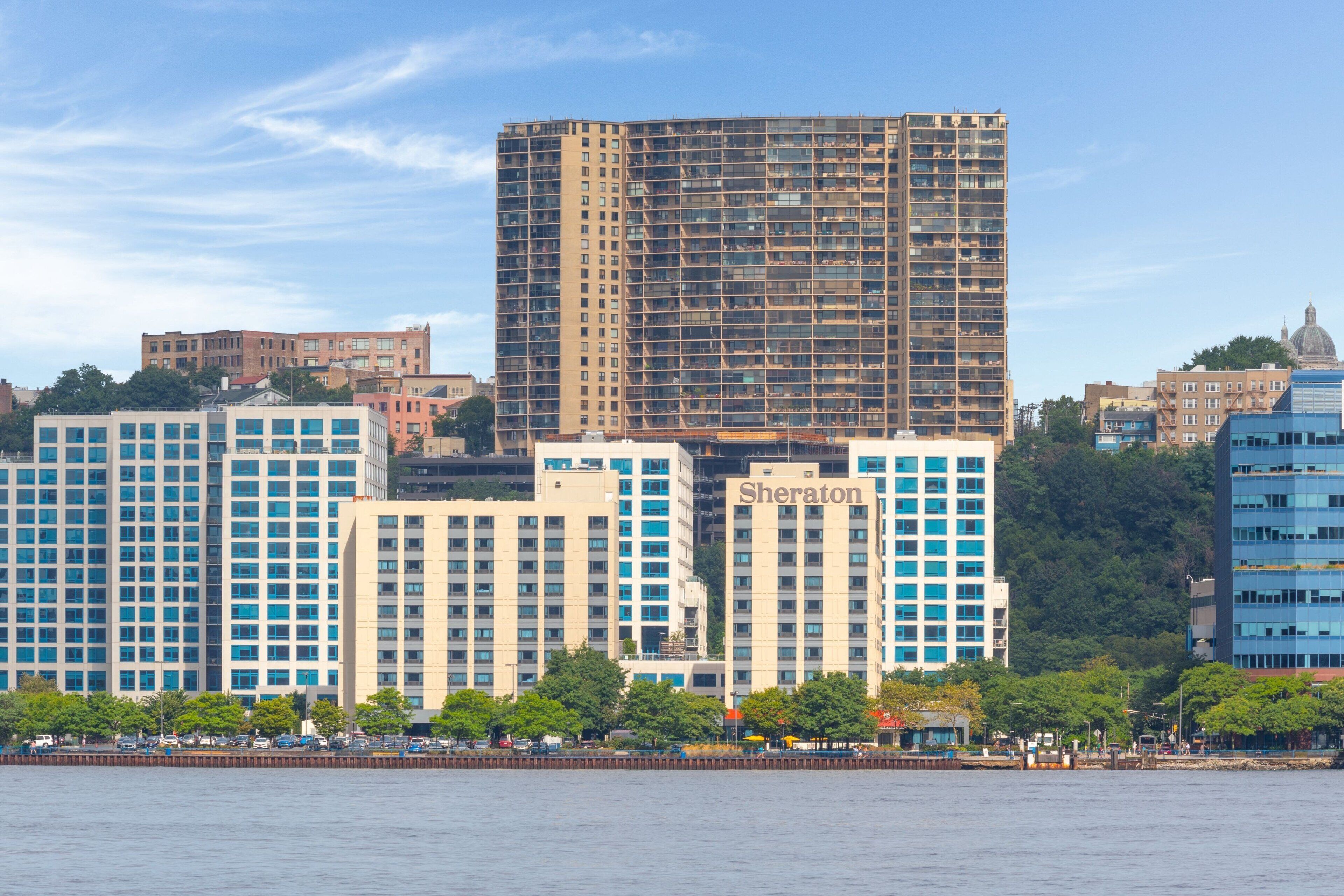 A high-rise hotel with a name sign, multiple floors, and a view of the city skyline across a body of water.