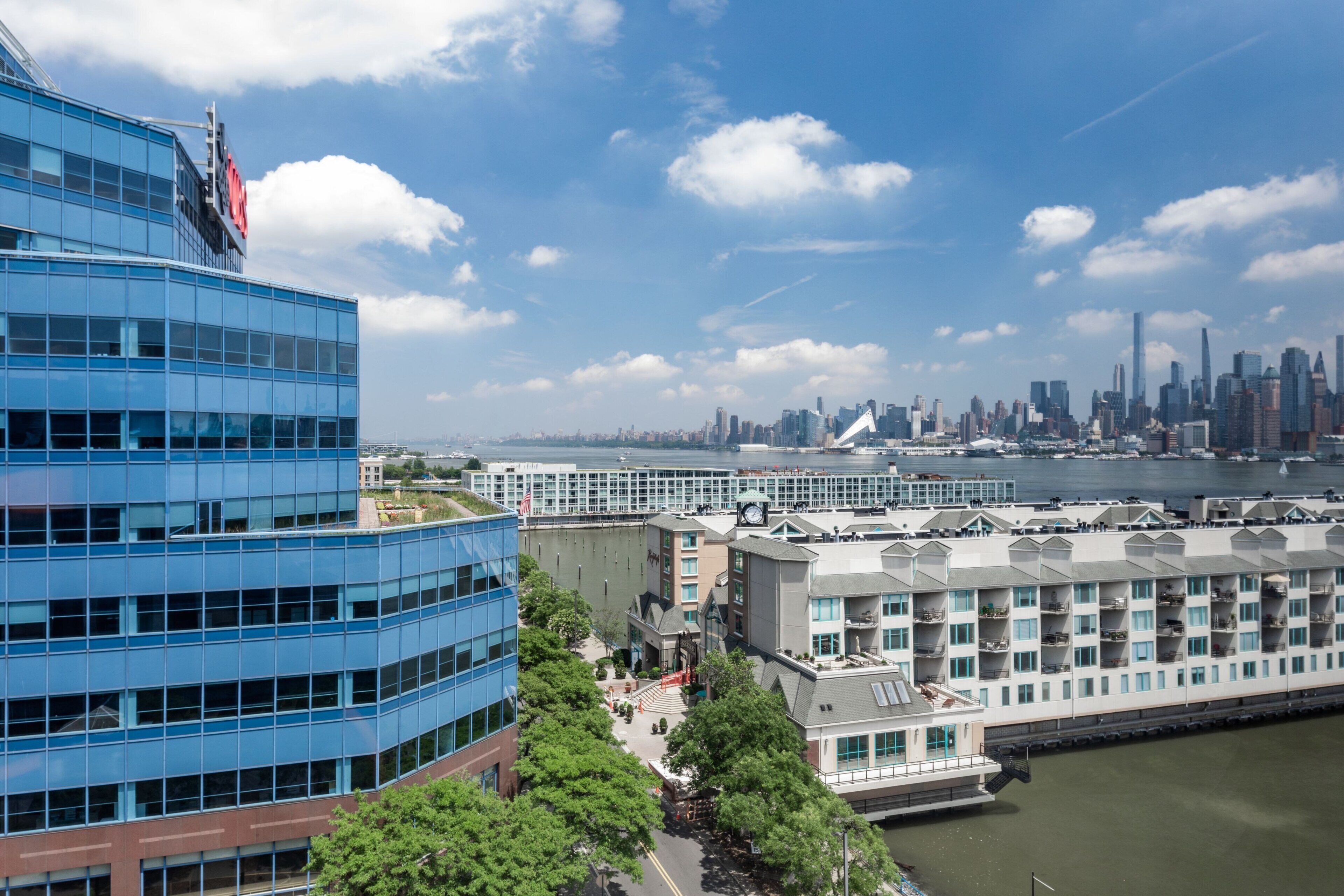 A modern hotel with a waterfront view, featuring a prominent clock tower and a large building with blue glass windows.