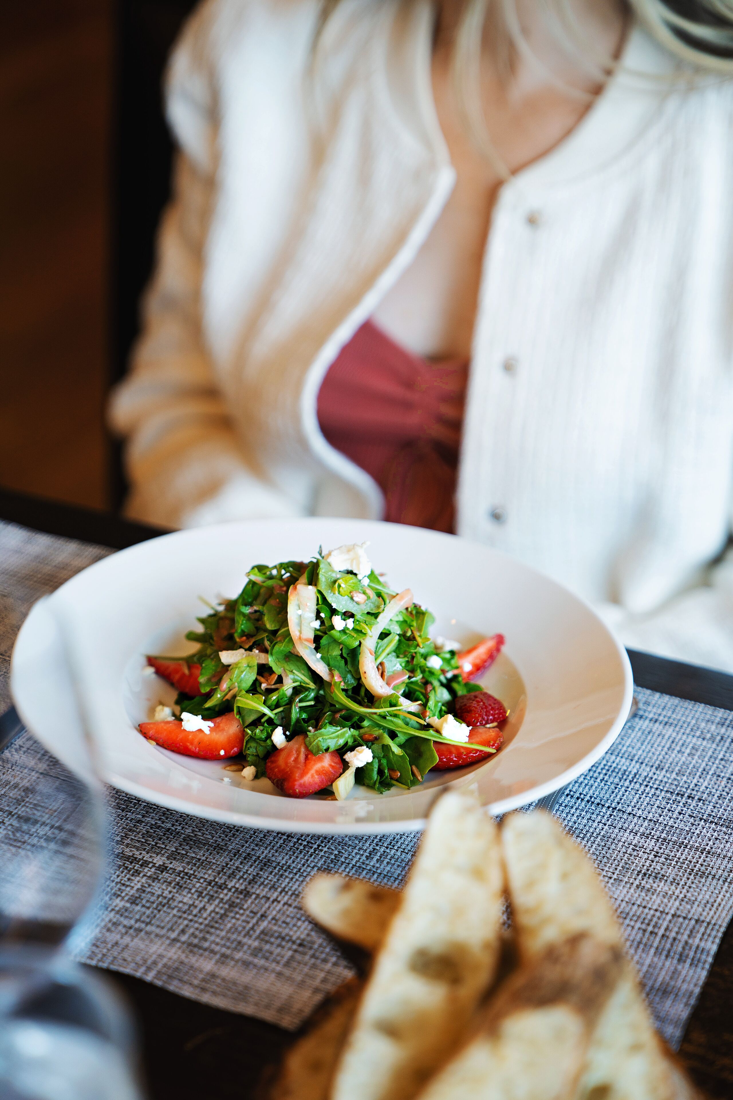 A white bowl of salad with strawberries and greens on a table with a gray cloth.