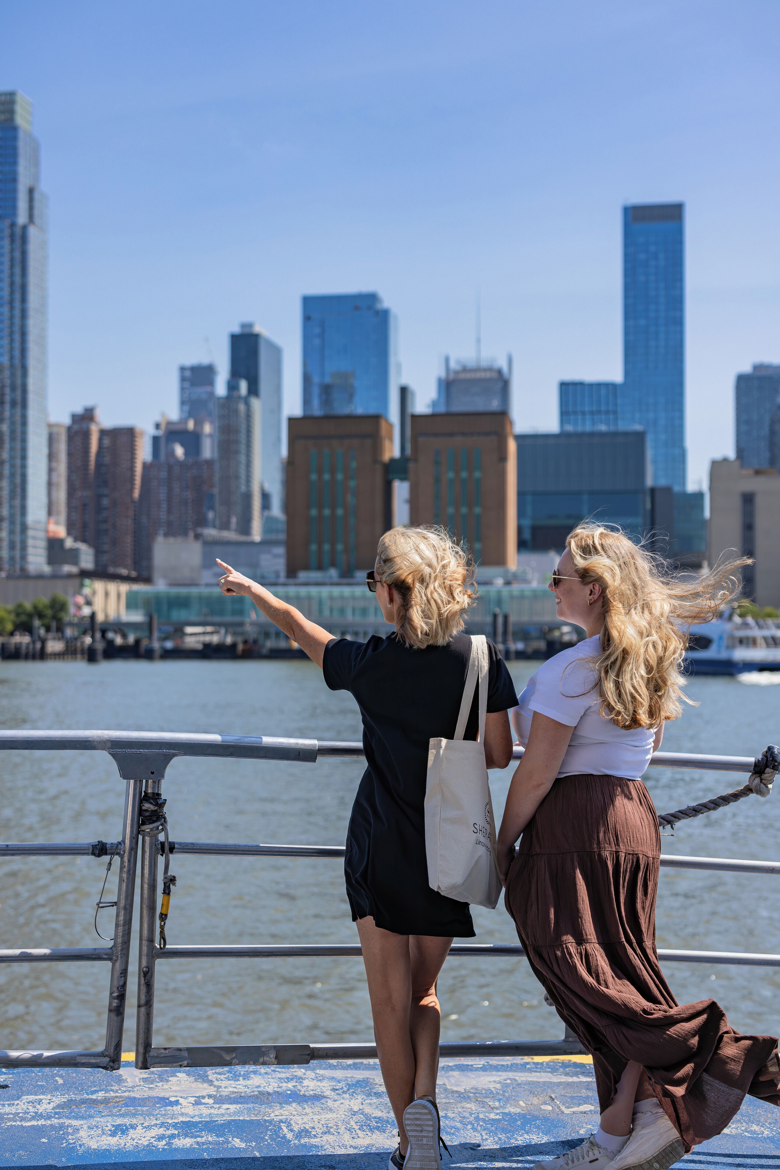 Two people standing by a waterfront with a city skyline in the background.