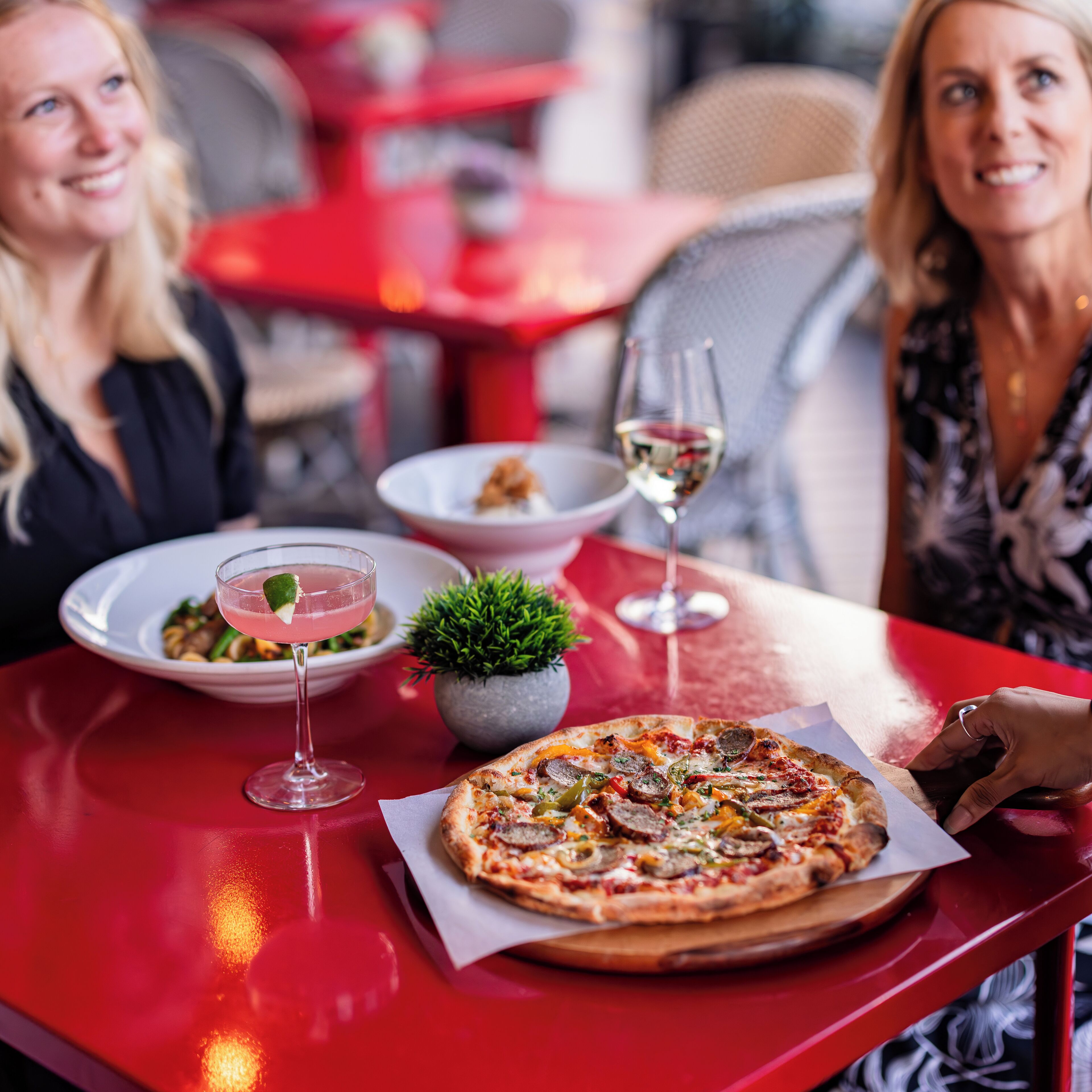 A dining table with a pizza, a salad, and two glasses of white wine.
