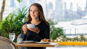 A person holding a cup at an outdoor table with a cityscape in the background.