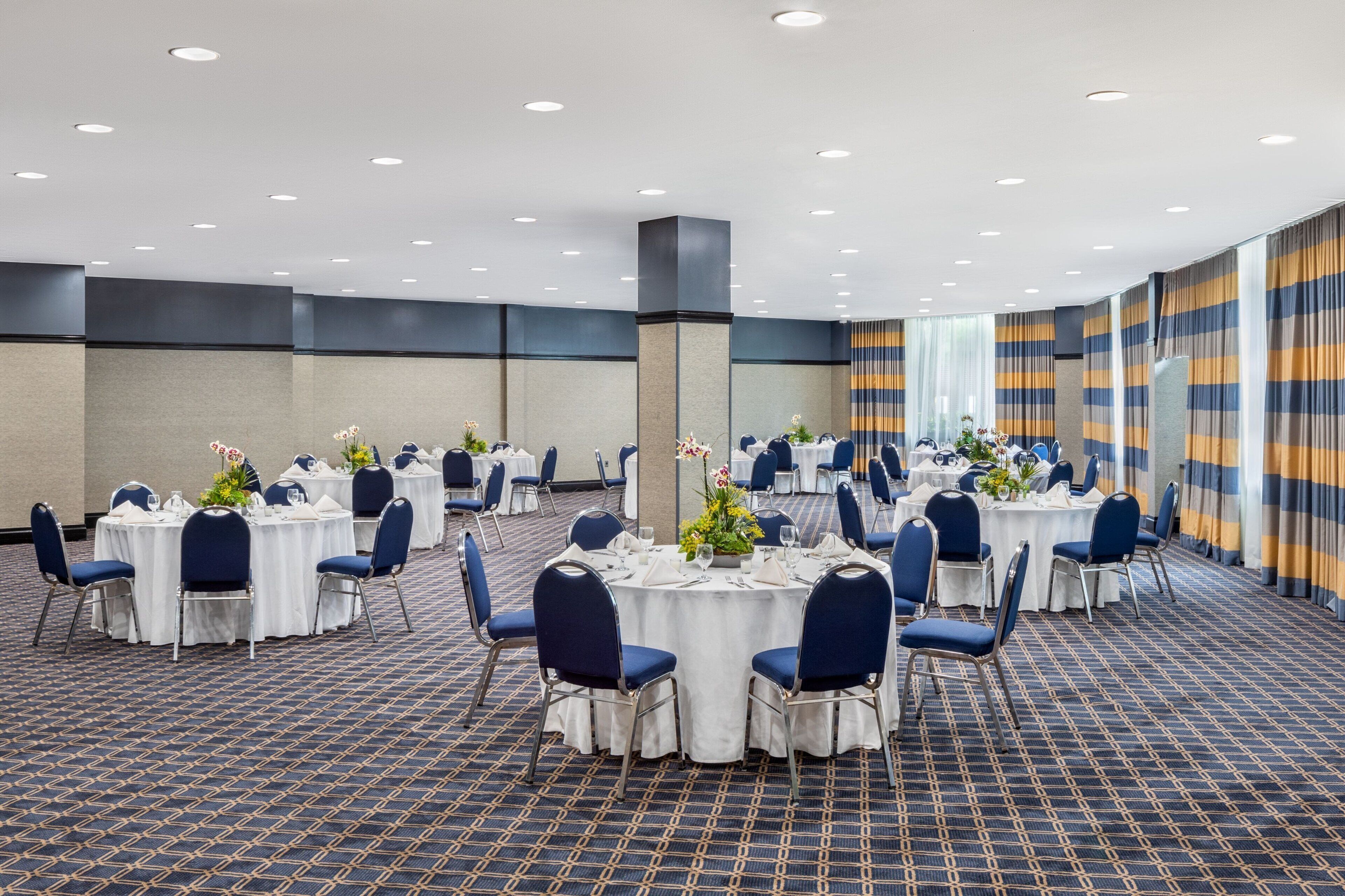 A conference room with round tables, blue chairs, and white tablecloths.