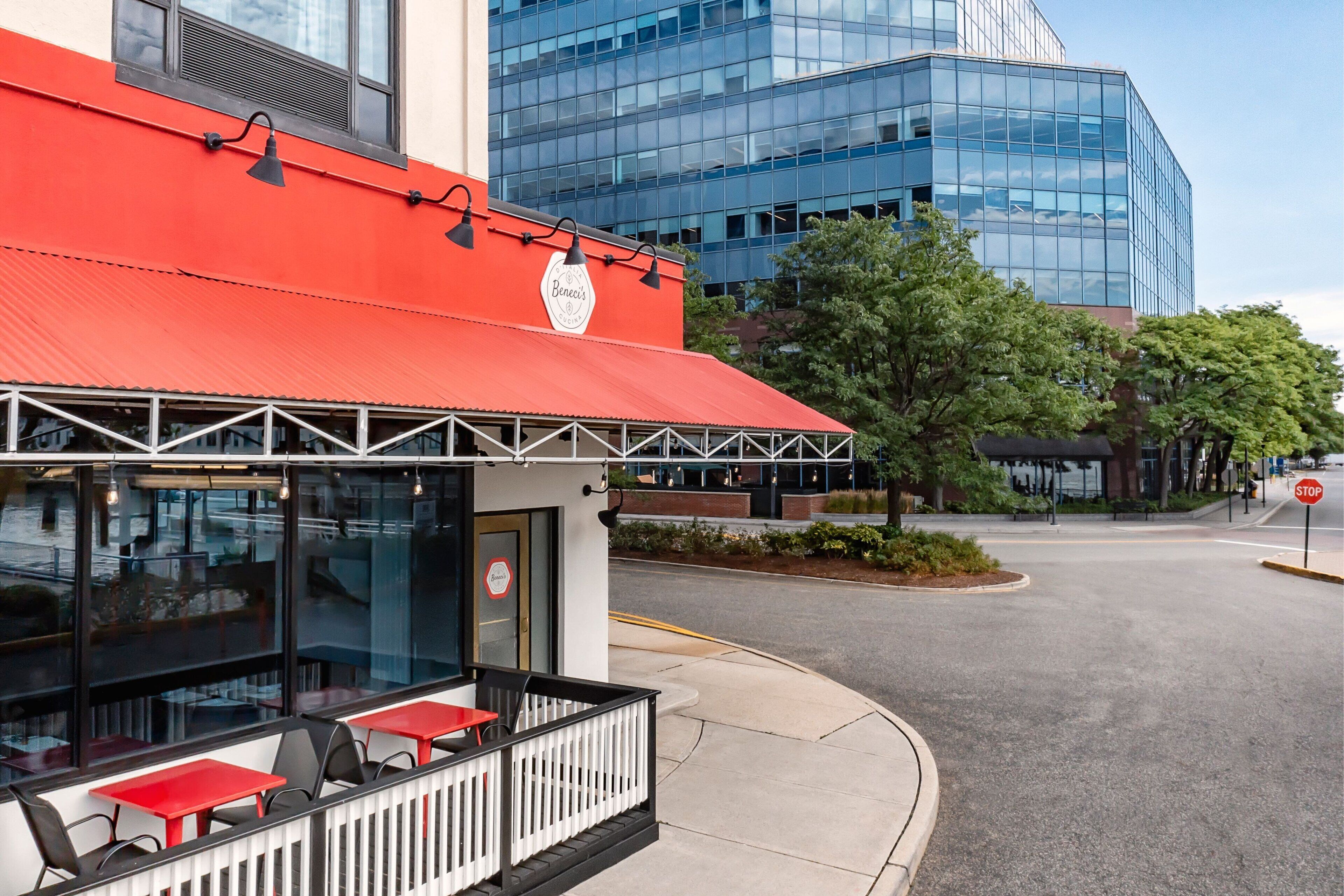 A restaurant with outdoor seating, a red awning, and a glass facade.