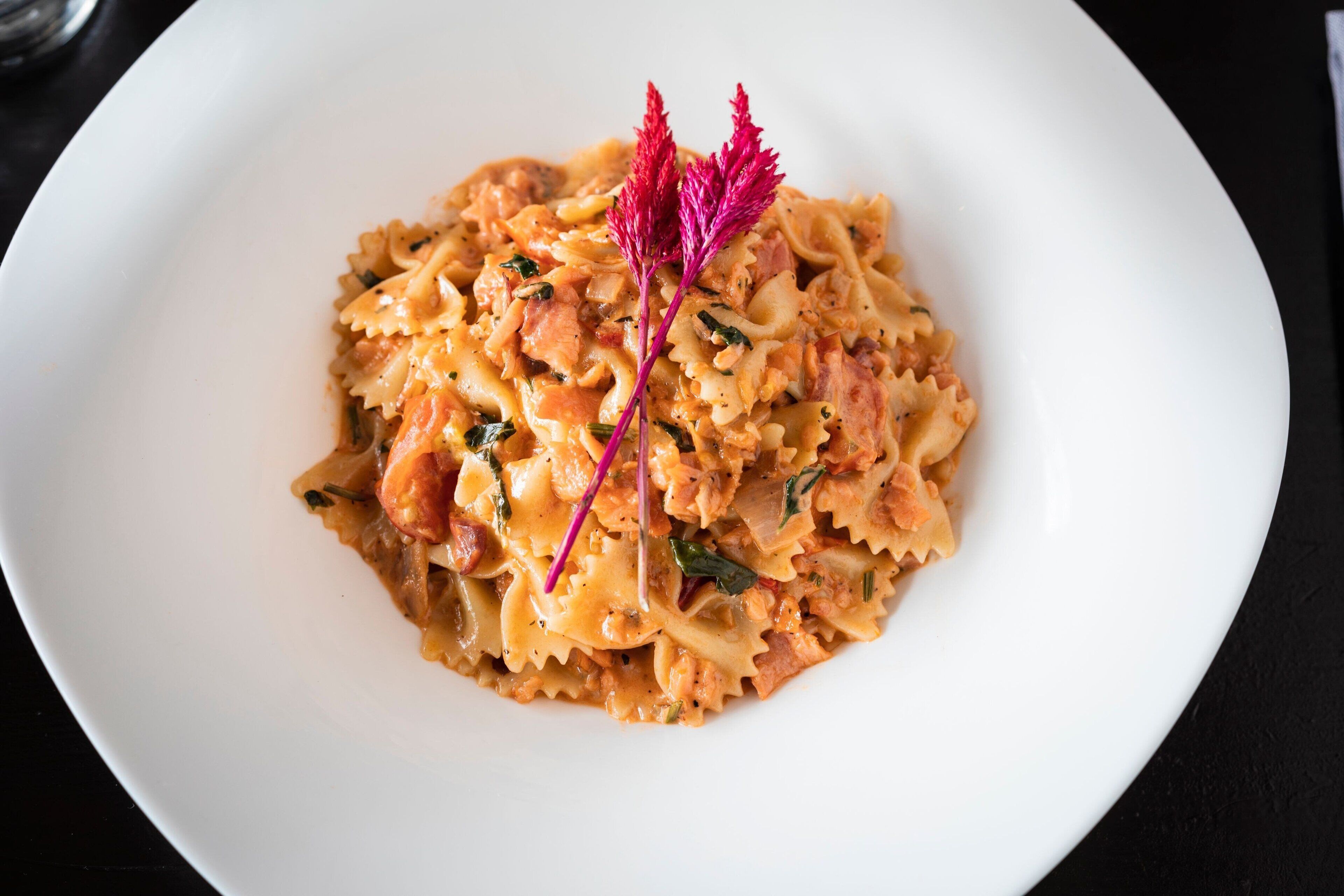 A white plate with pasta, garnished with a purple leaf.