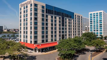 A Sheraton hotel with a modern glass facade, a red awning, and a parking lot with trees.