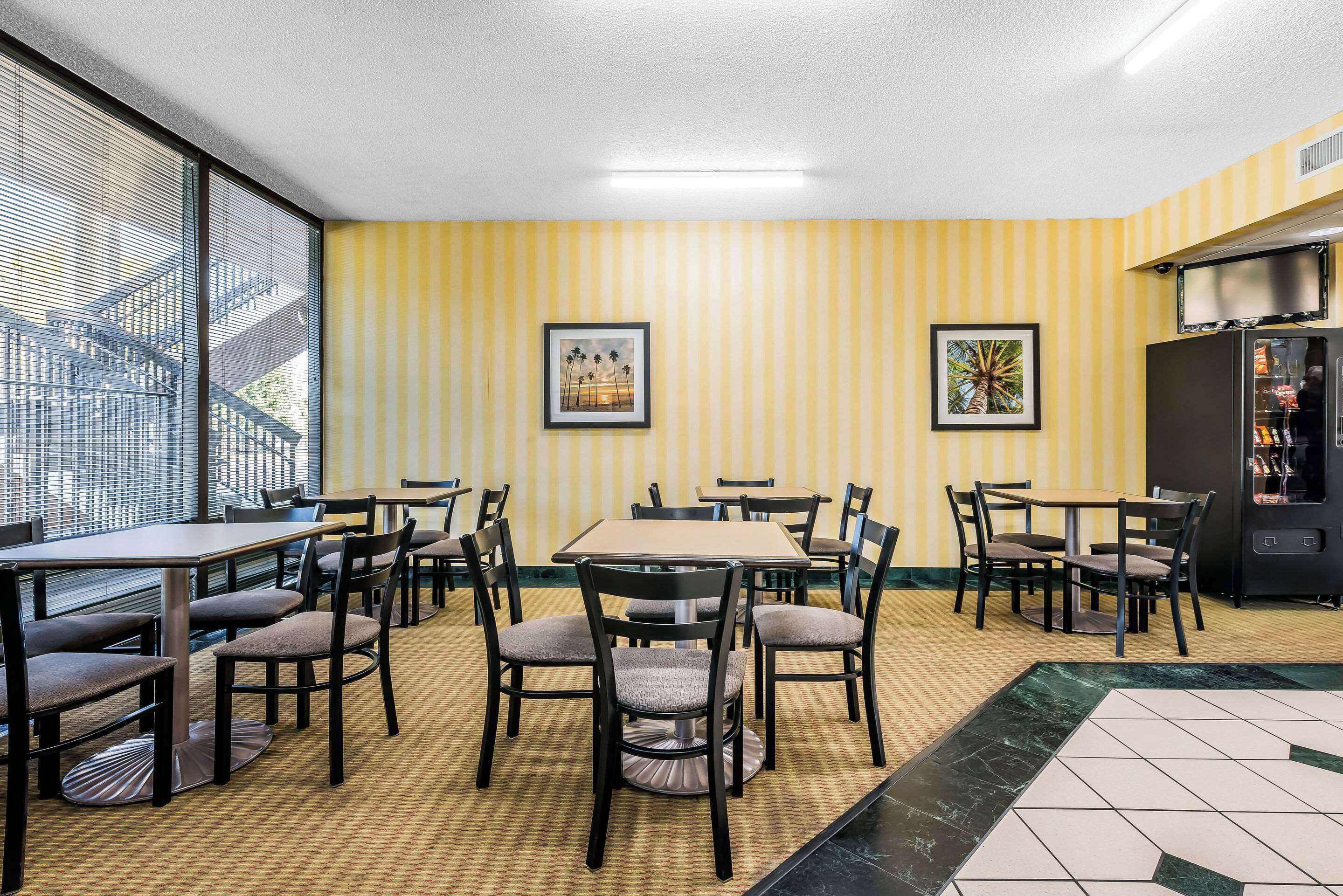 A dining area with striped yellow walls, multiple tables and chairs, and framed artwork on the walls.