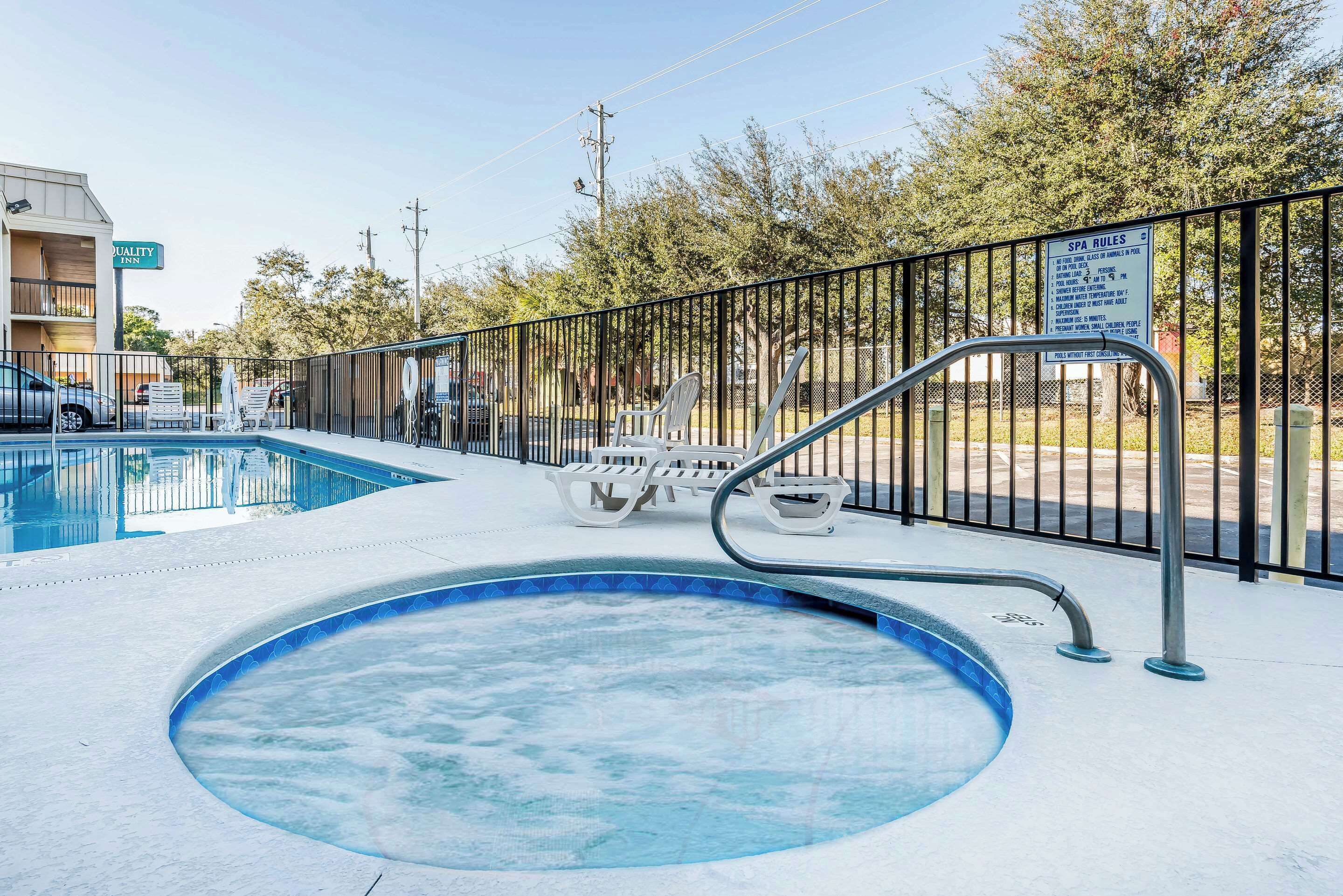 A swimming pool with a metal fence, lounge chairs, and a sign indicating spa rules.