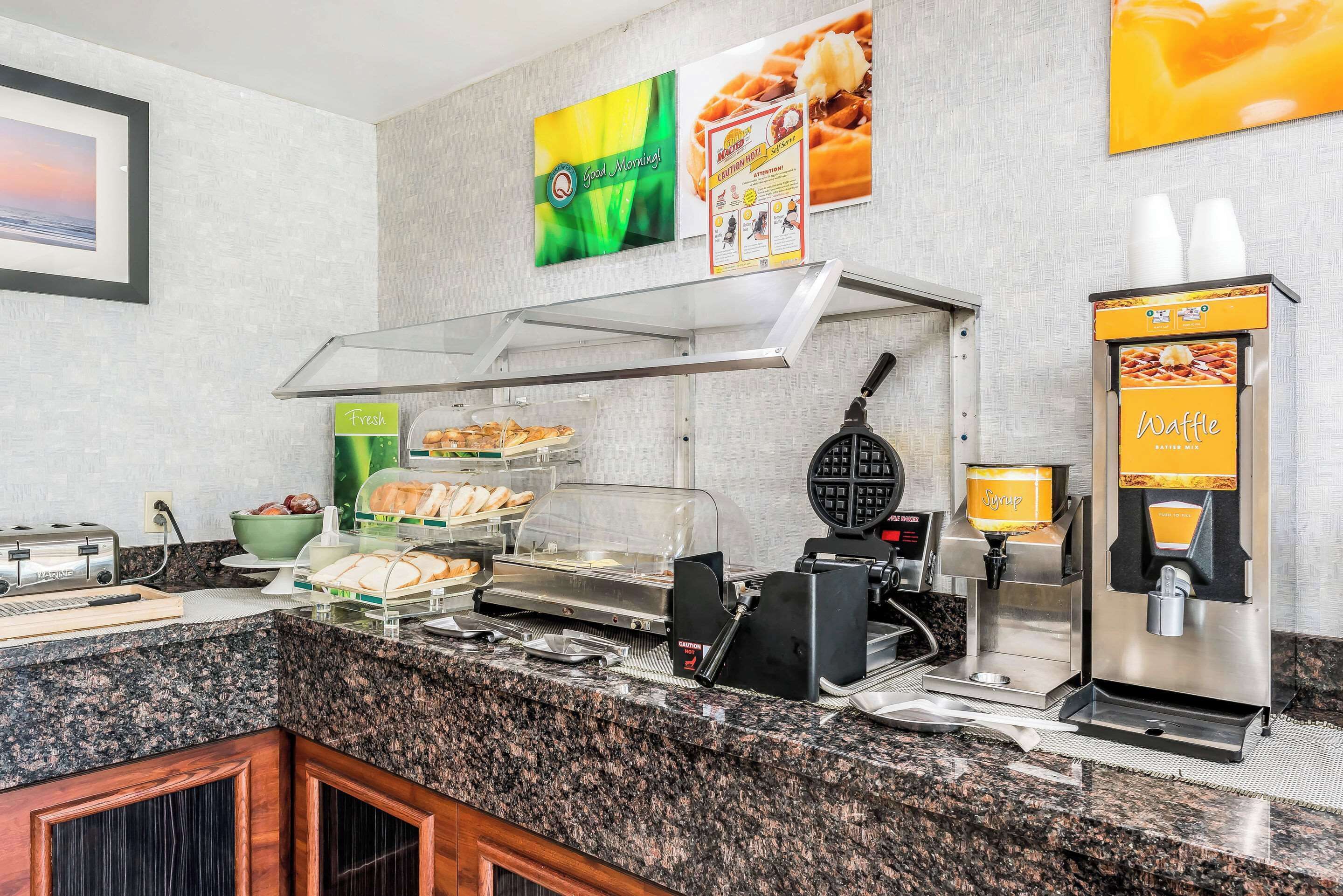 A breakfast bar with a waffle maker, syrup dispenser, and a coffee machine.
