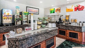 Zona de desayuno de hotel con mostrador de granito, dispensadores de jugo y diversas opciones de comida.