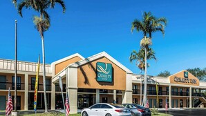 Hotel Quality Inn con diseño moderno, que muestra un logotipo destacado, varias banderas y un estacionamiento con automóviles.