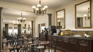 A spacious dining area with multiple tables and chairs, a large chandelier, and a bar area with a mirror and wine bottles. - Victorian Inn (Monterey)