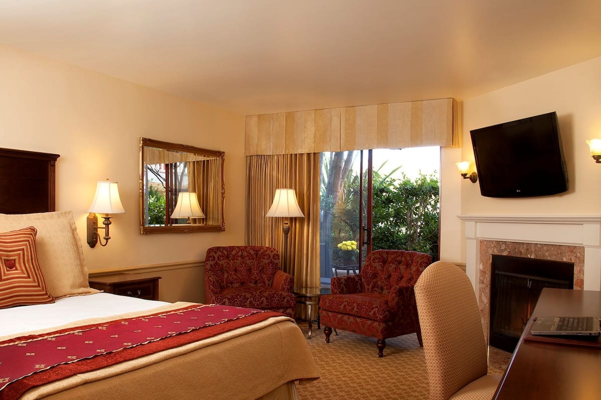 A hotel room with a bed, two armchairs, a TV, and a fireplace.