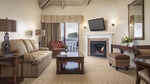A living room with a sofa, armchair, ottoman, coffee table, fireplace, television, and a large mirror. - Victorian Inn (Monterey)
