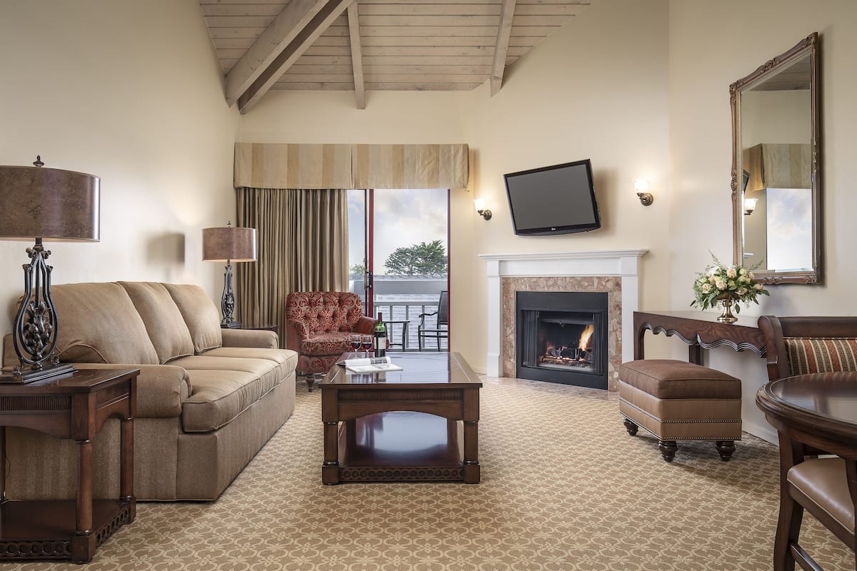 A living room with a sofa, armchair, ottoman, coffee table, fireplace, television, and a large mirror.