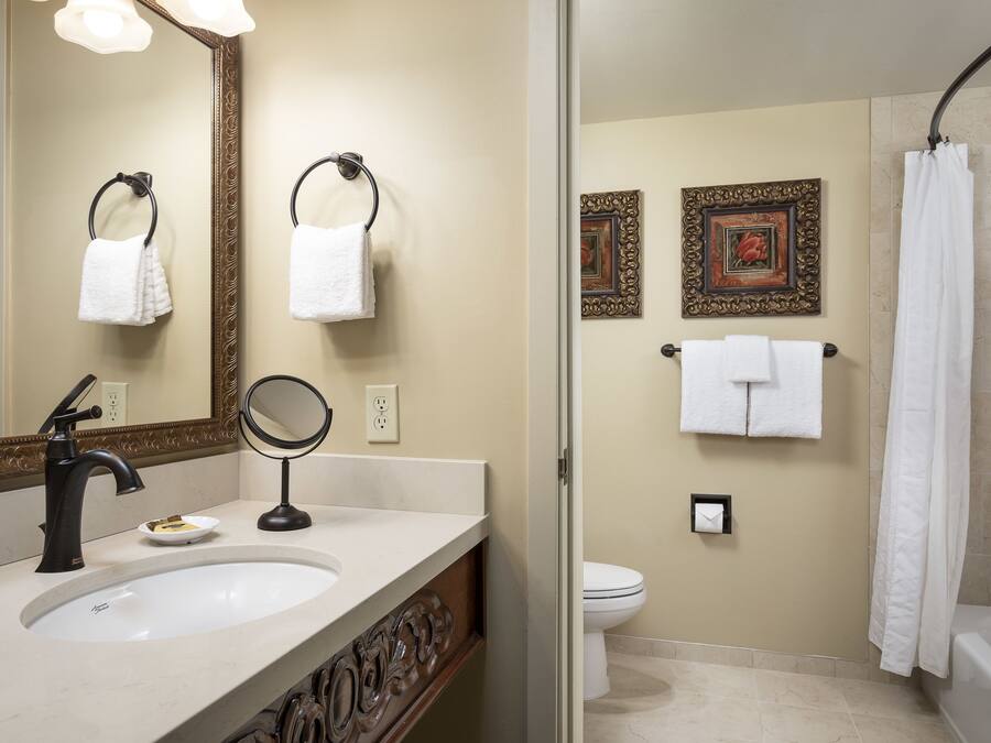 A bathroom with a sink, mirror, towel rings, toilet, and a shower curtain.