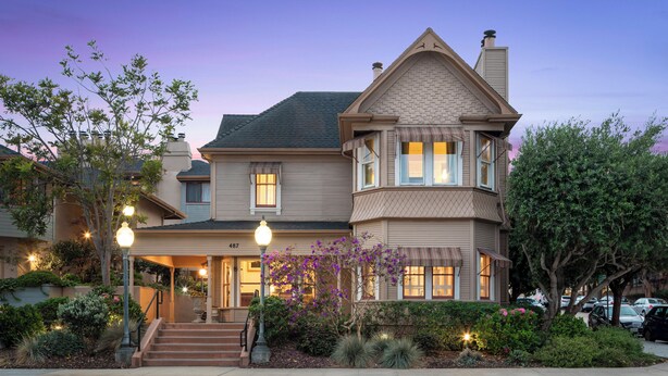 A two-story house with a wrap-around porch, a chimney, and a well-maintained garden. - Victorian Inn (Monterey)