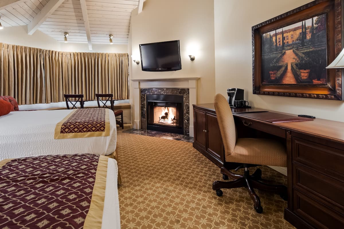A hotel room with a bed, a desk, a fireplace, a TV, and a painting.