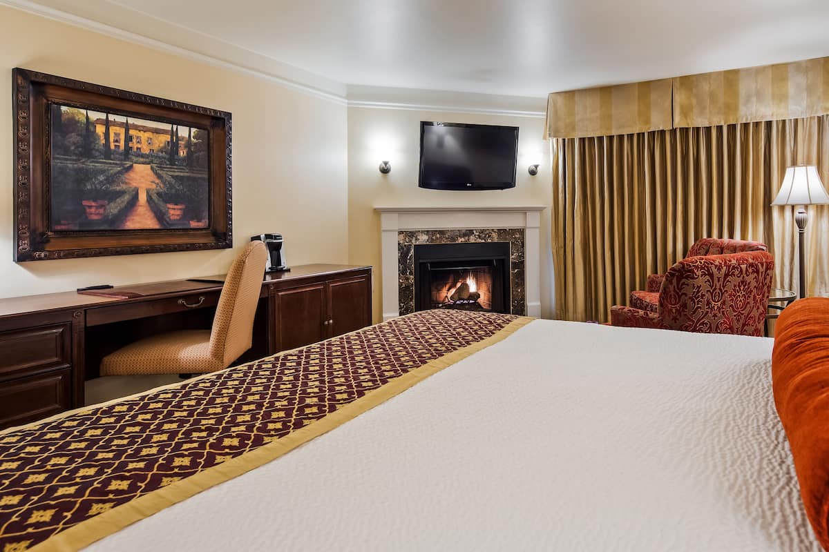 A hotel room with a bed, a desk, a chair, a fireplace, a television, and a window with curtains.
