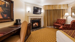 A hotel room with a fireplace, a television, a desk with a coffee maker, and a comfortable seating area with a patterned carpet. - Victorian Inn (Monterey)