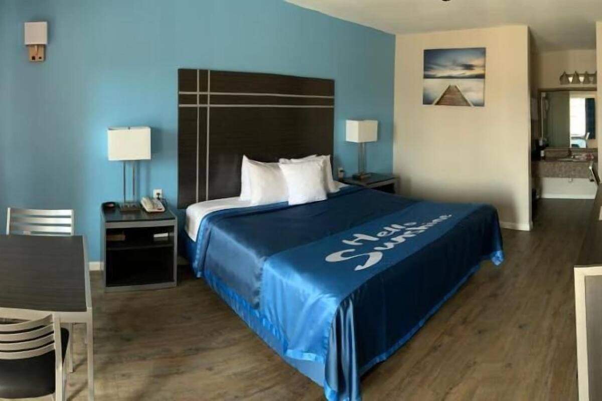 Ett hotellrum med en säng, ett skrivbord, en stol, sängbord och utsikt över köket.
