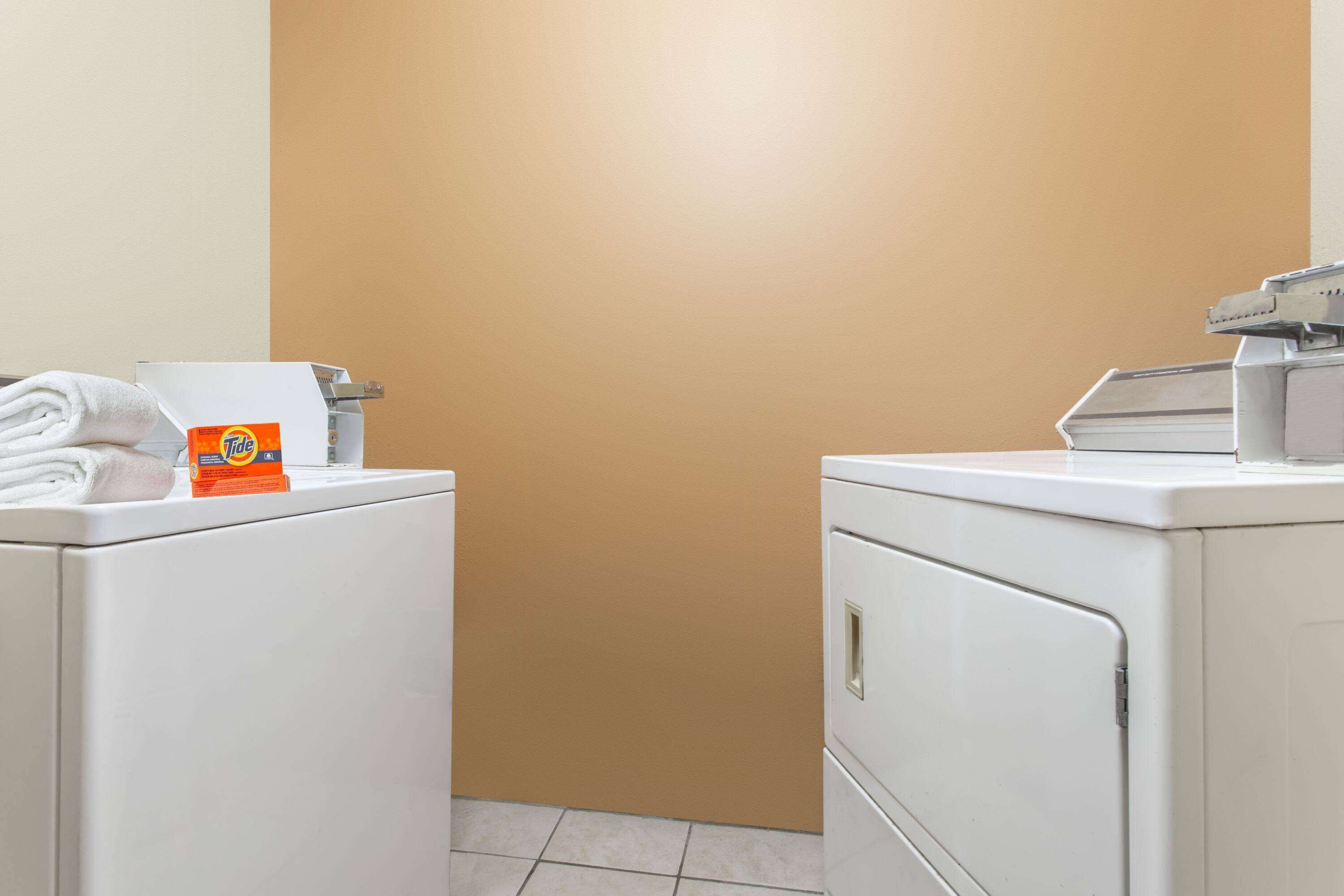 A laundry area with two white washing machines, a towel, and a Tide detergent box.