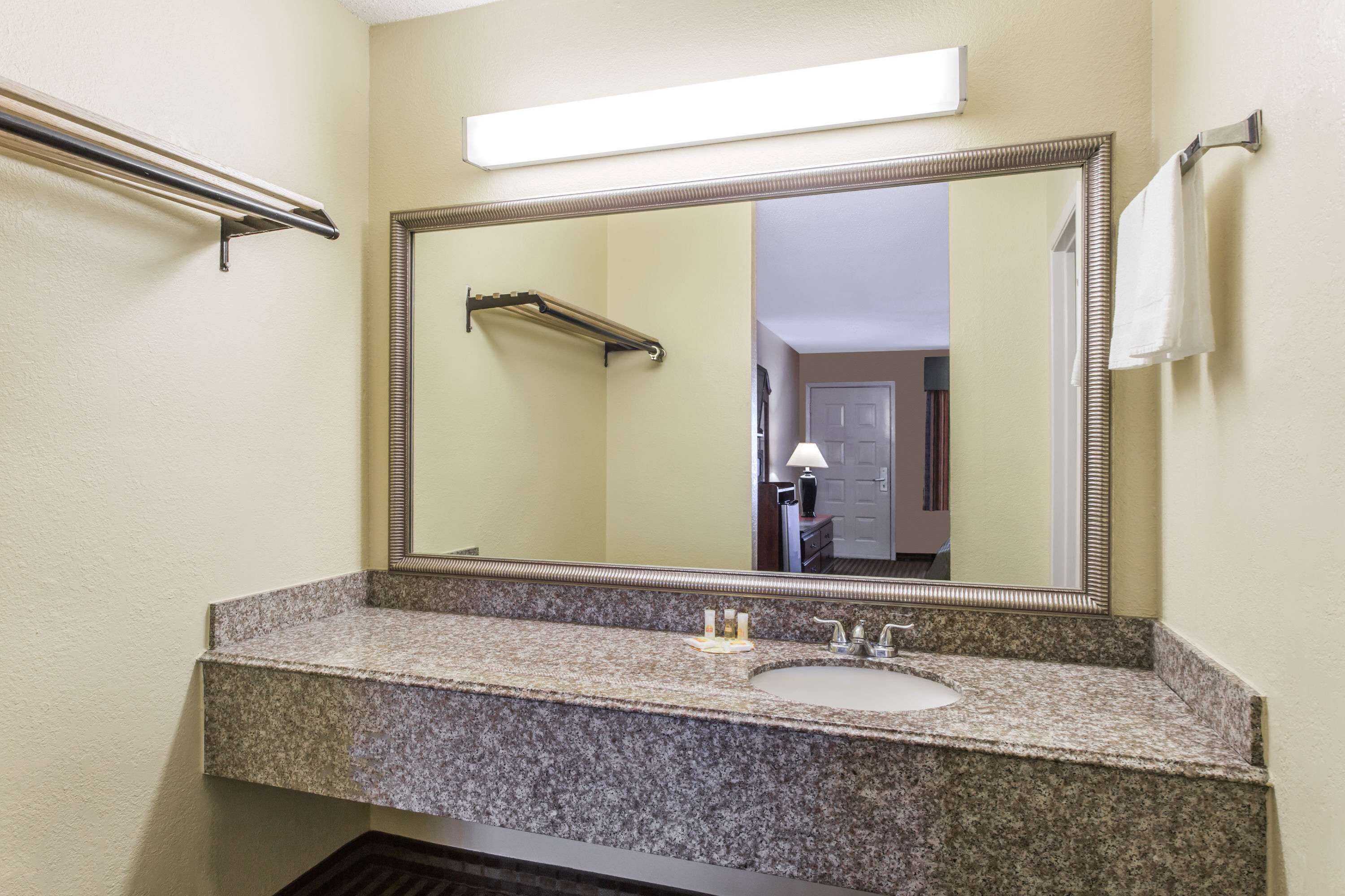 A bathroom with a granite countertop, a sink, a mirror, and a towel rack.