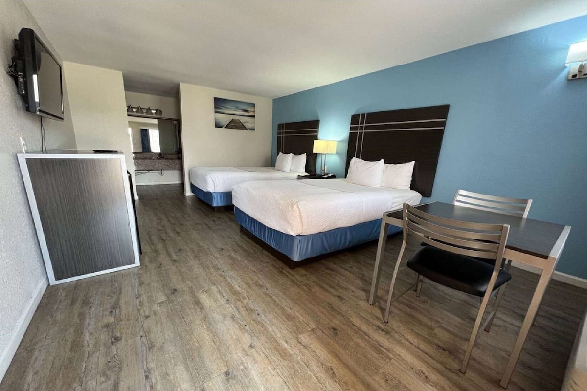 Ett hotellrum med två sängar, ett skrivbord, en stol, en TV och ett litet pentry.