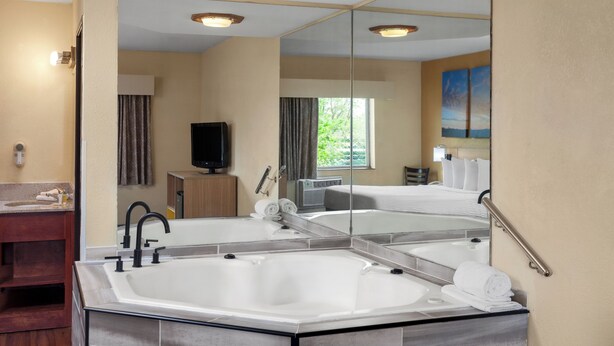 A modern bathroom with a large bathtub, a vanity with a mirror, and a television. - Days Inn by Wyndham Rockford I-90 Casino District (Rockford)