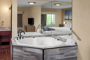 A modern bathroom with a large bathtub, a vanity with a mirror, and a television. - Days Inn by Wyndham Rockford I-90 Casino District (Rockford)