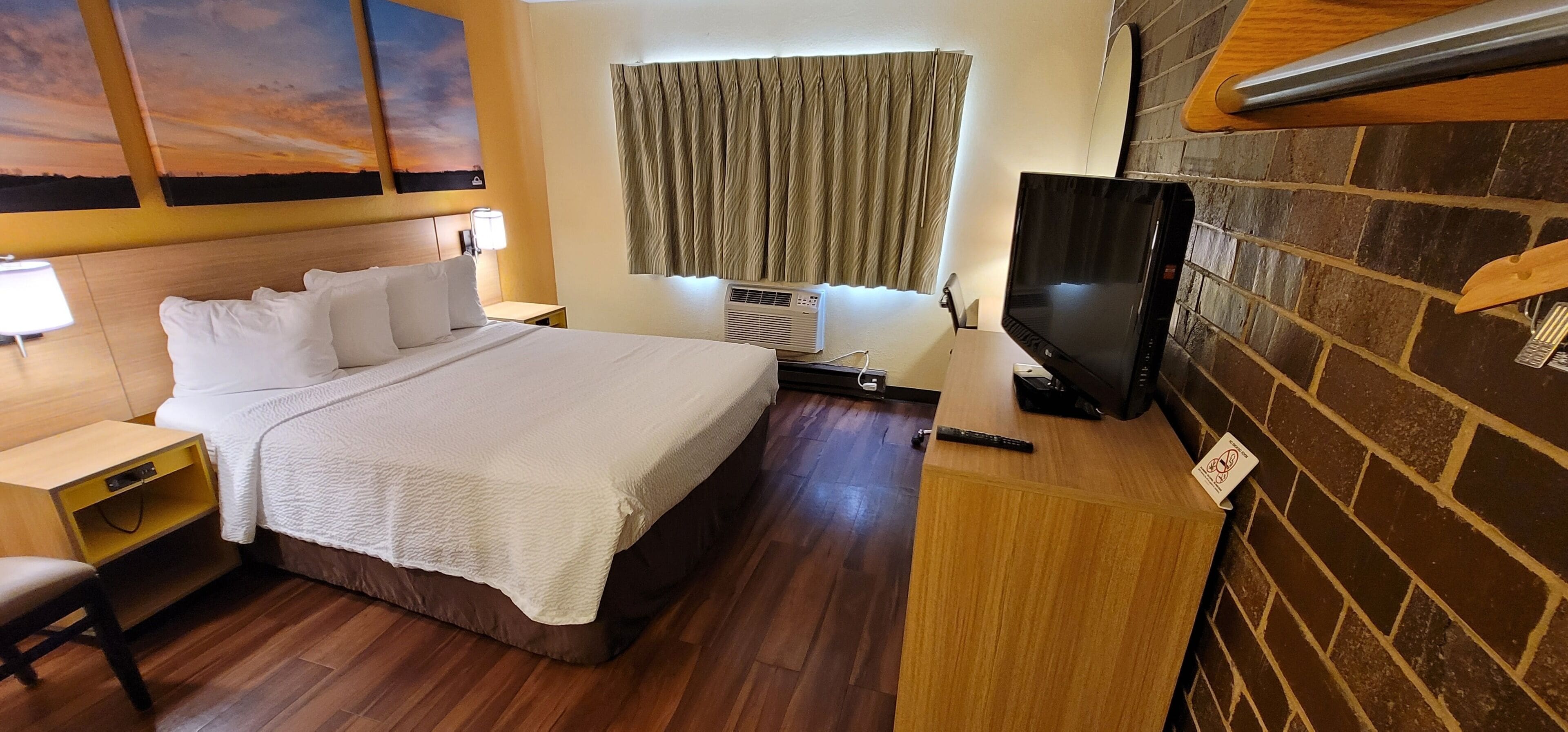 Una habitación de hotel con una cama, un escritorio, un televisor y una pared de ladrillo.