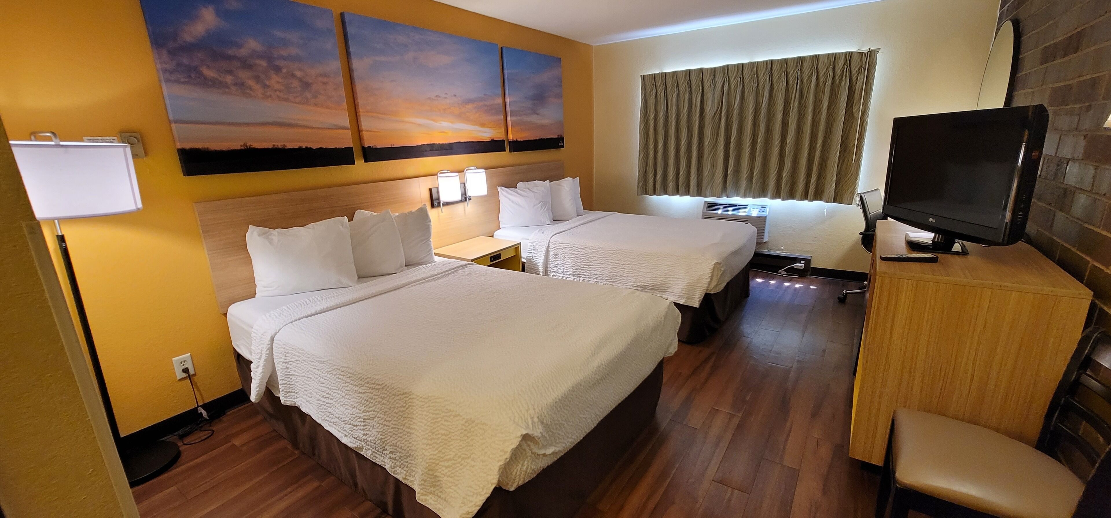 A hotel room with two beds, a television, a desk, and a window with curtains.