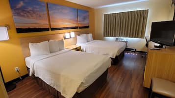 A hotel room with two beds, a television, a desk, and a window with curtains.